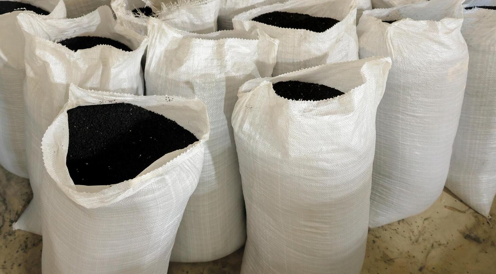 Rows of open white sacks filled with black rubber granules at Bedrock's plant